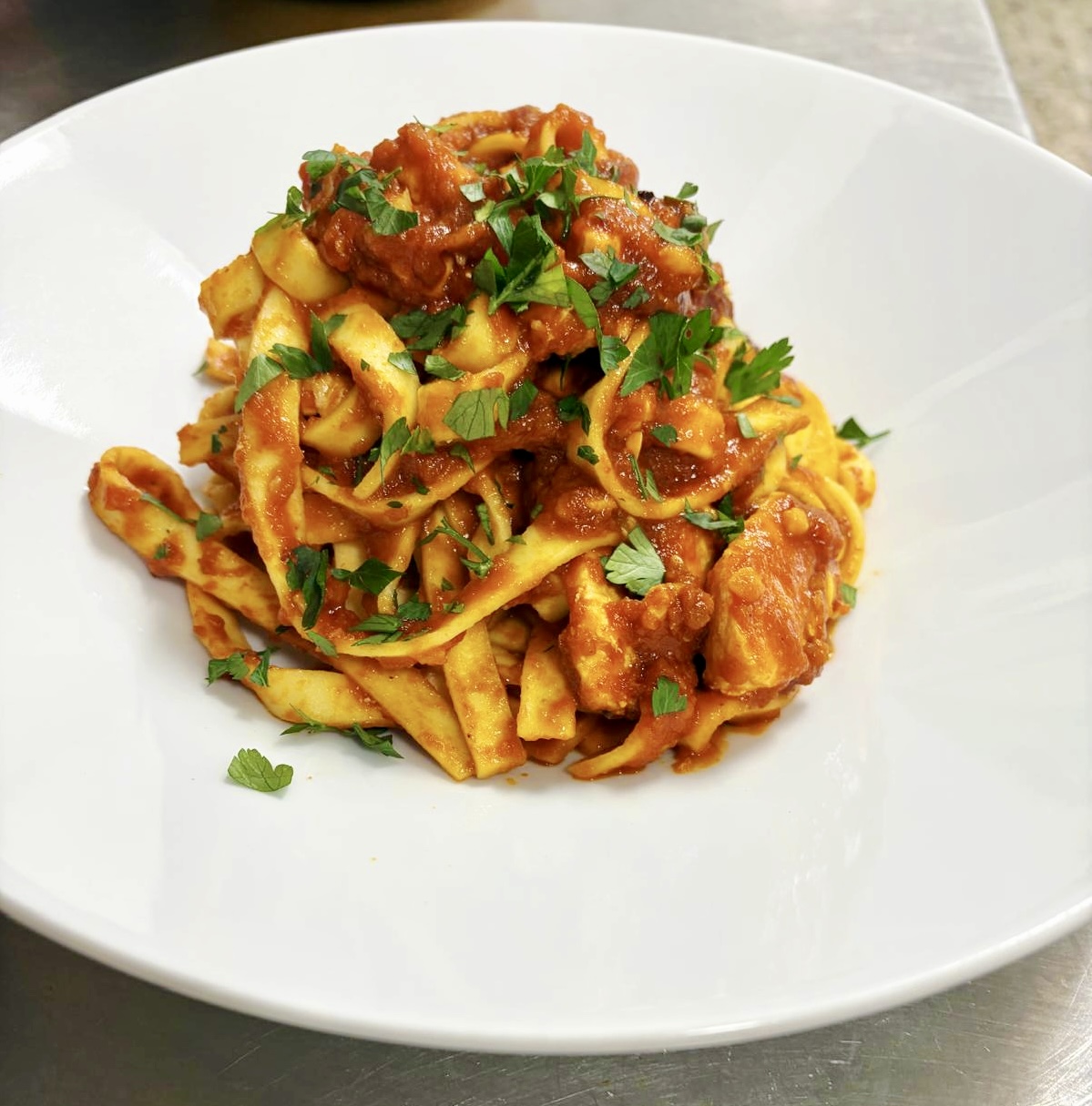 Bandnudeln mit roter Sauce und frischen Kräutern auf einem weißen Teller