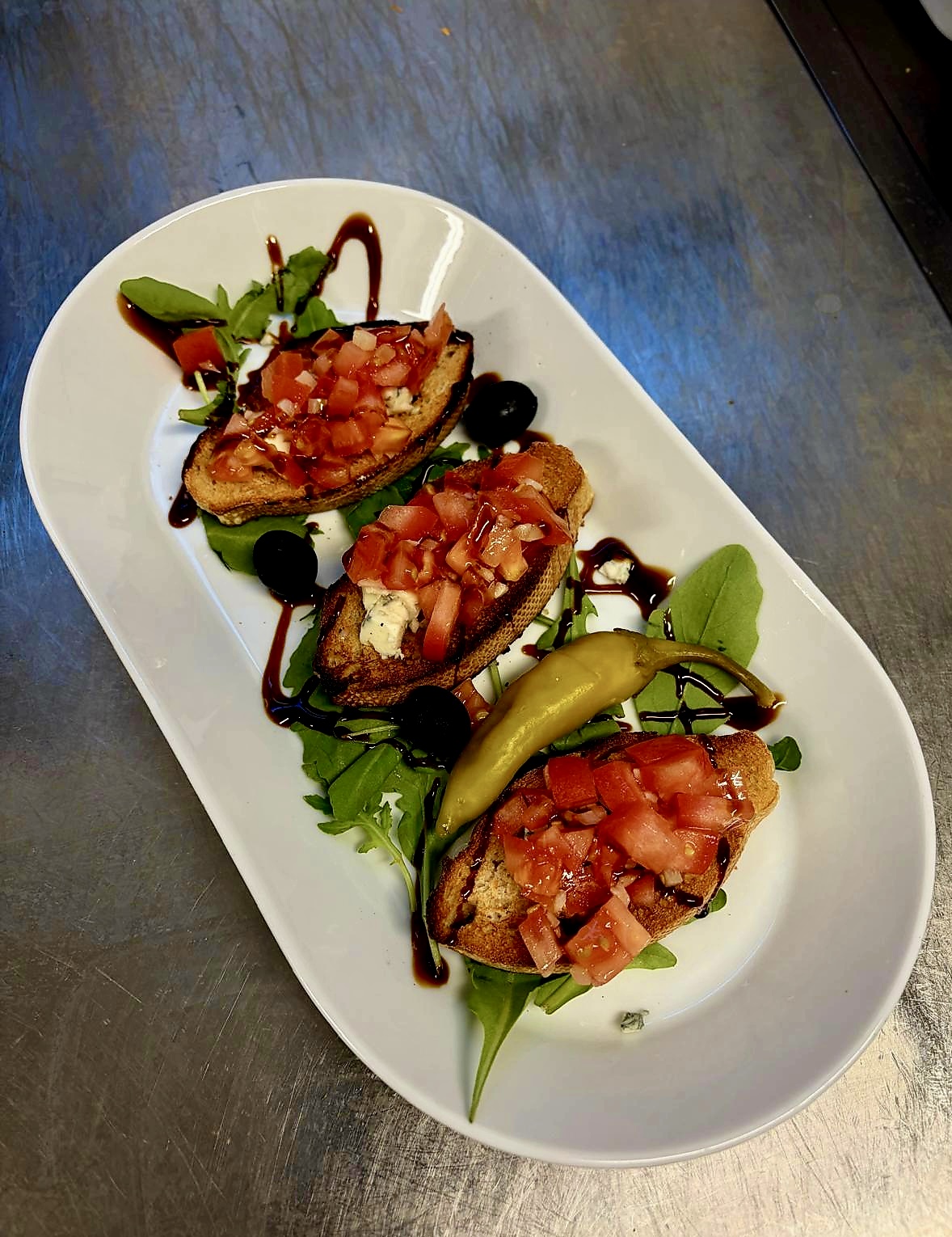 Drei geröstete Brotscheiben mit Tomaten auf einem länglichen Teller