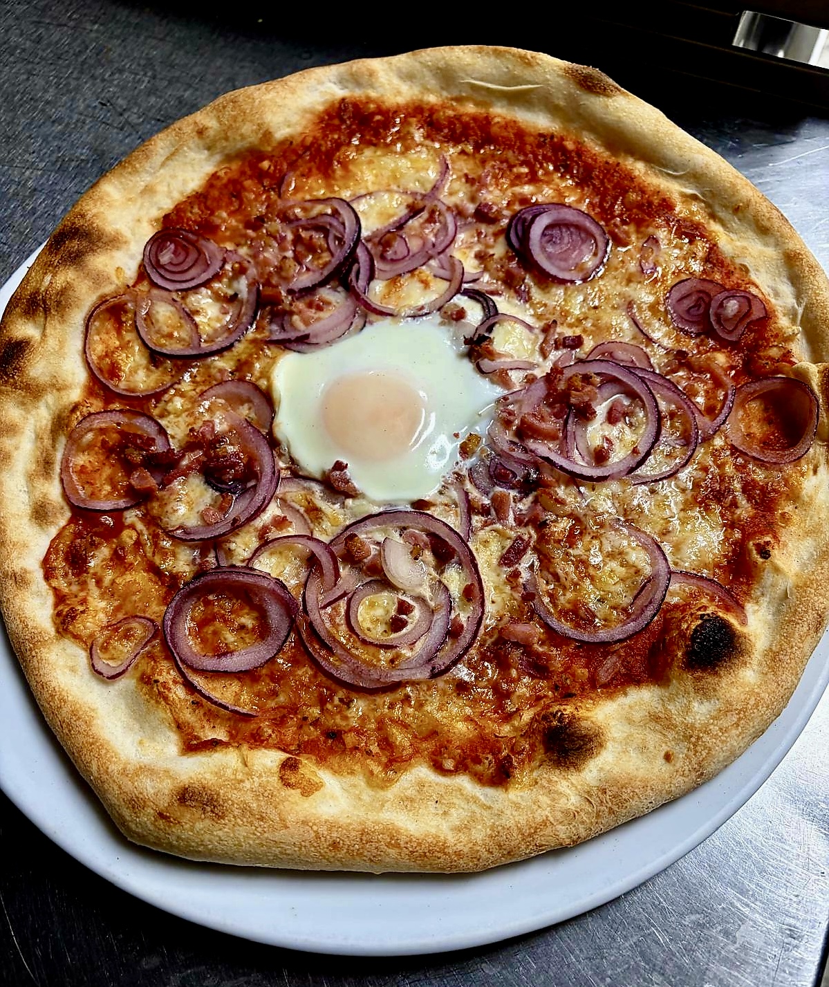 Frisch gebackene Pizza mit roten Zwiebeln und Ei aus der Küche der Pizzeria Schwanen
