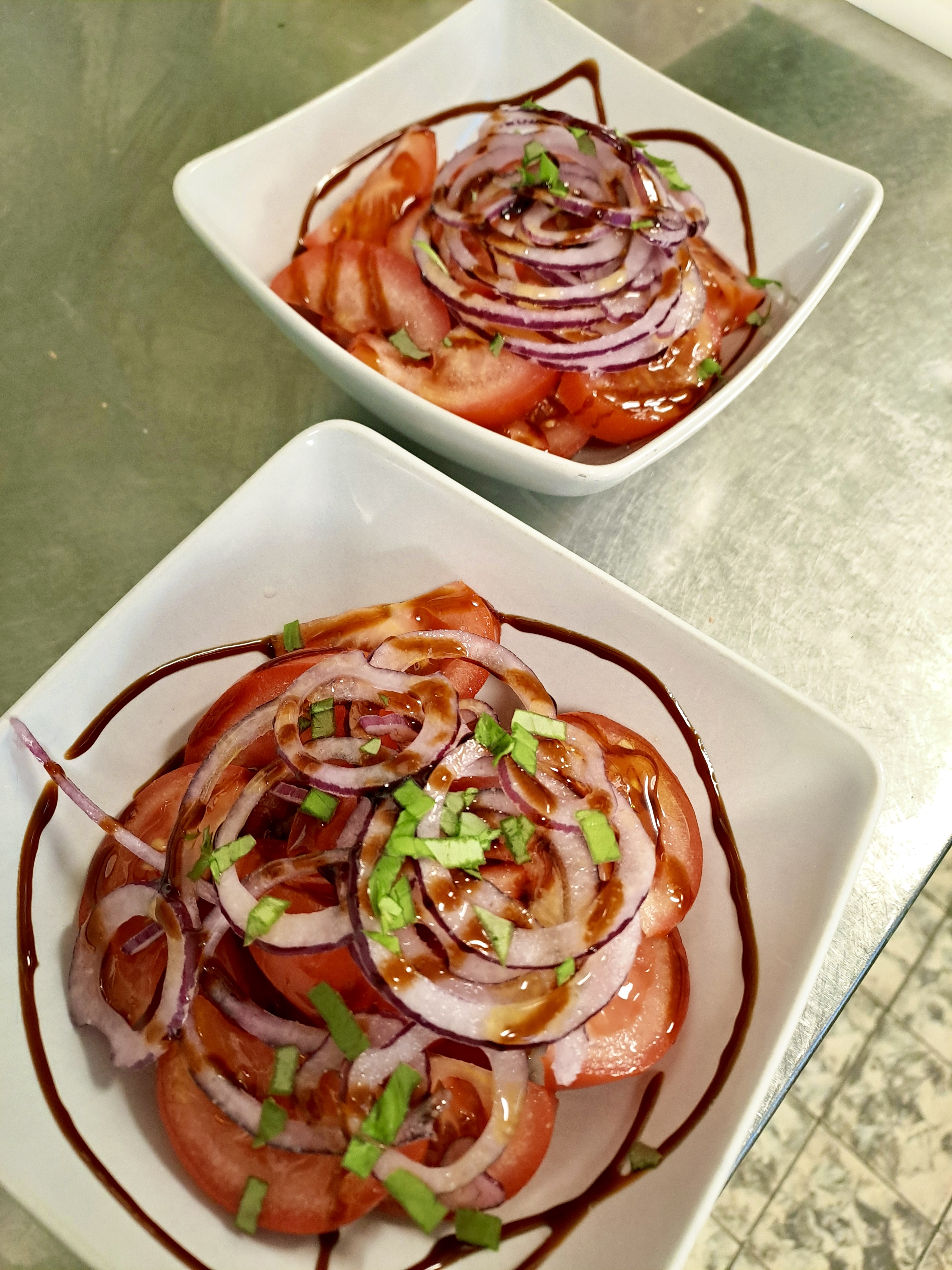Tomatensalat mit roten Zwiebeln und Kräutern in weißen Schalen