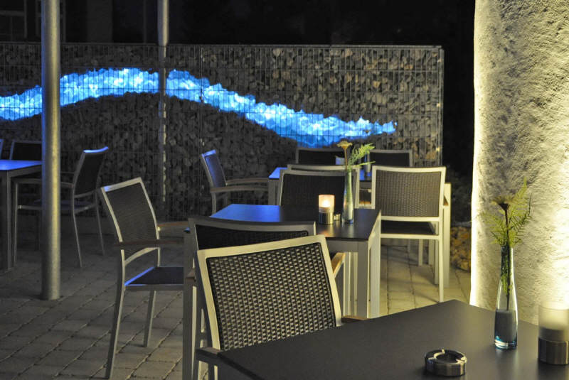 Sitzplätze auf der Terrasse mit beleuchteter Steinwand am Abend